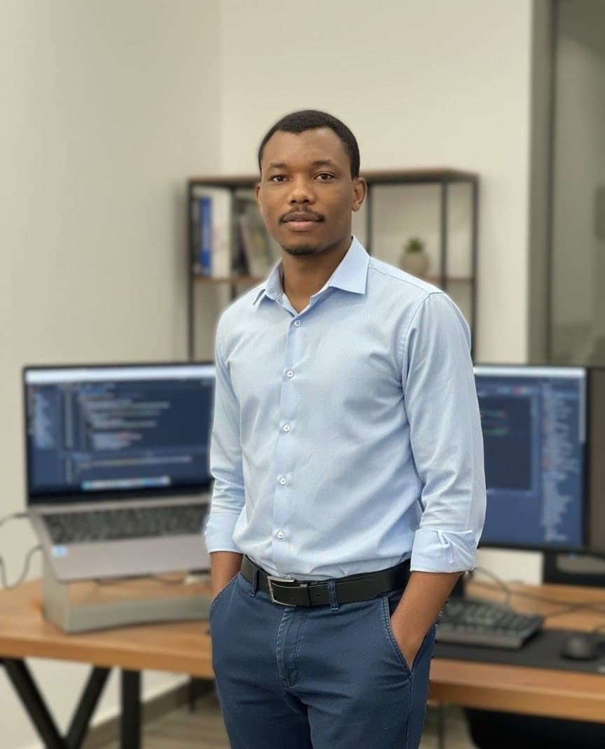 Micheal Macaulay standing in front of two monitors showing code